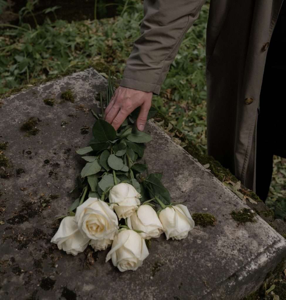 mano de hombre con flores blancas sobre una tumba